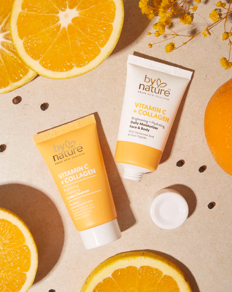 uckland product photography of By Nature Vitamin C + Collagen Cream Cleanser and Daily Moisturiser styled in a flat lay with fresh orange slices, yellow wattle flowers, and black peppercorns, by Amanda Hughes Photography.