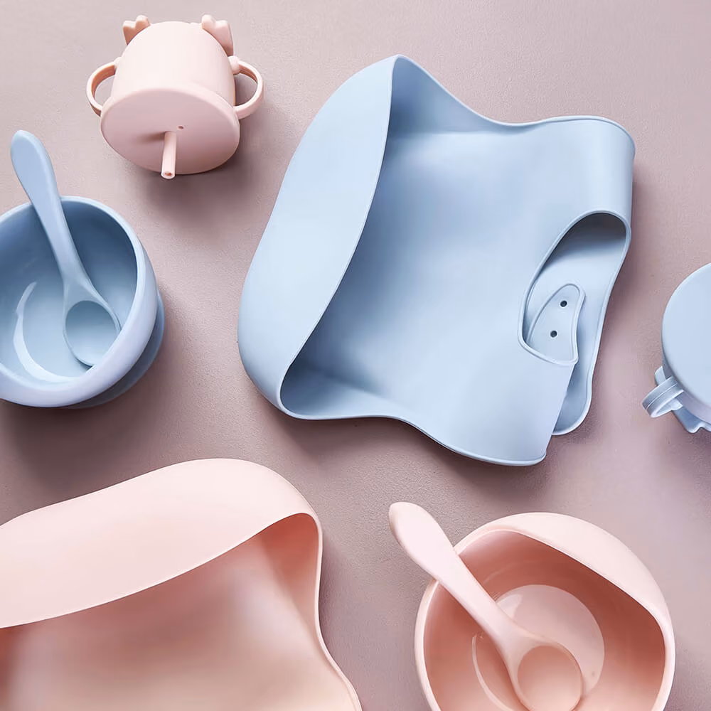 Auckland product photography of a silicone baby feeding set including bibs, suction bowls, spoons, and a sippy cup in pastel pink and blue, styled in a flat la…Auckland product photography of a silicone baby feeding set including bibs, suction bowls, spoons, and a sippy cup in pastel pink and blue, styled in a flat lay by Amanda Hughes Photography.