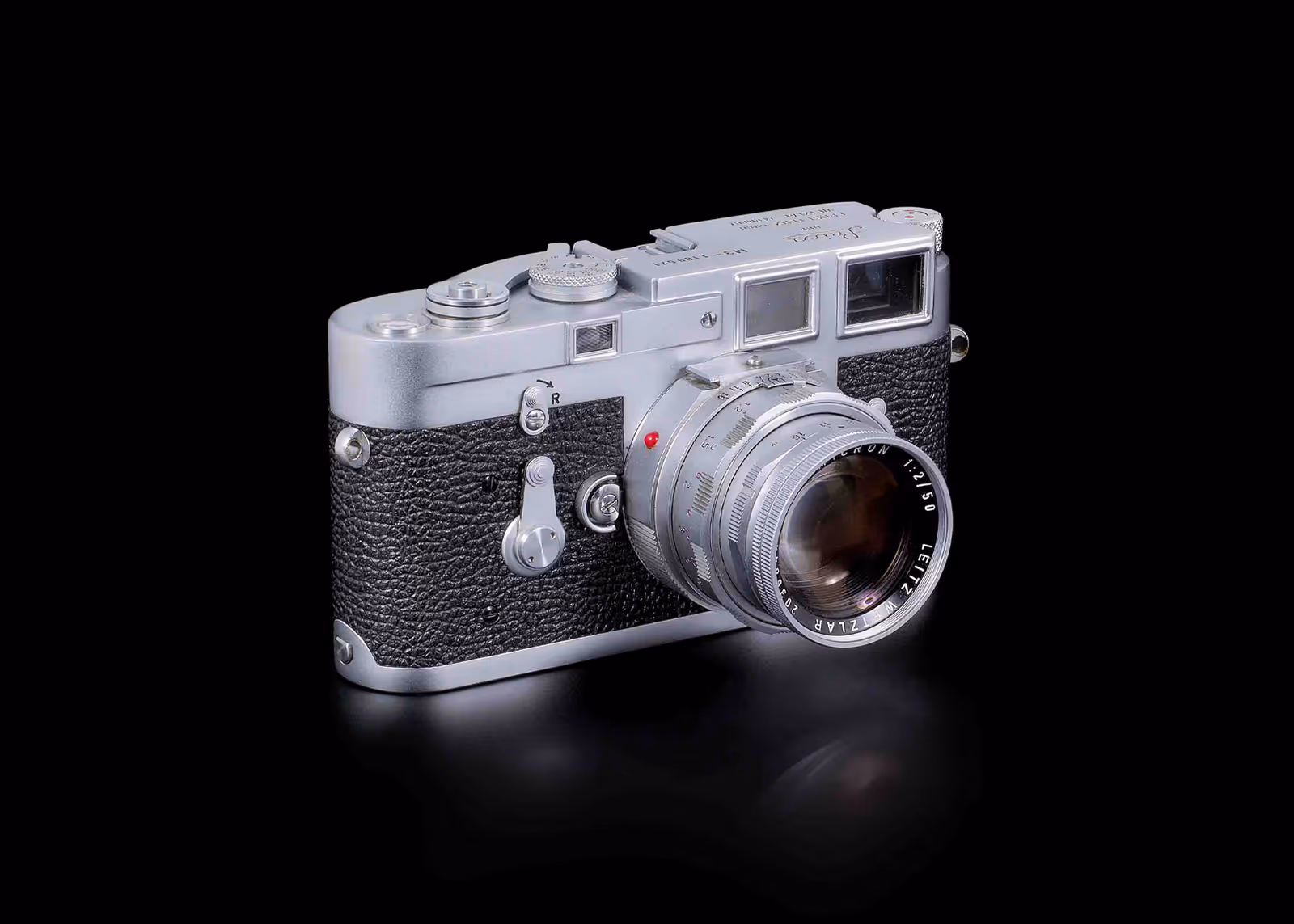 Vintage silver Leica camera with textured black grip and attached lens on black background.