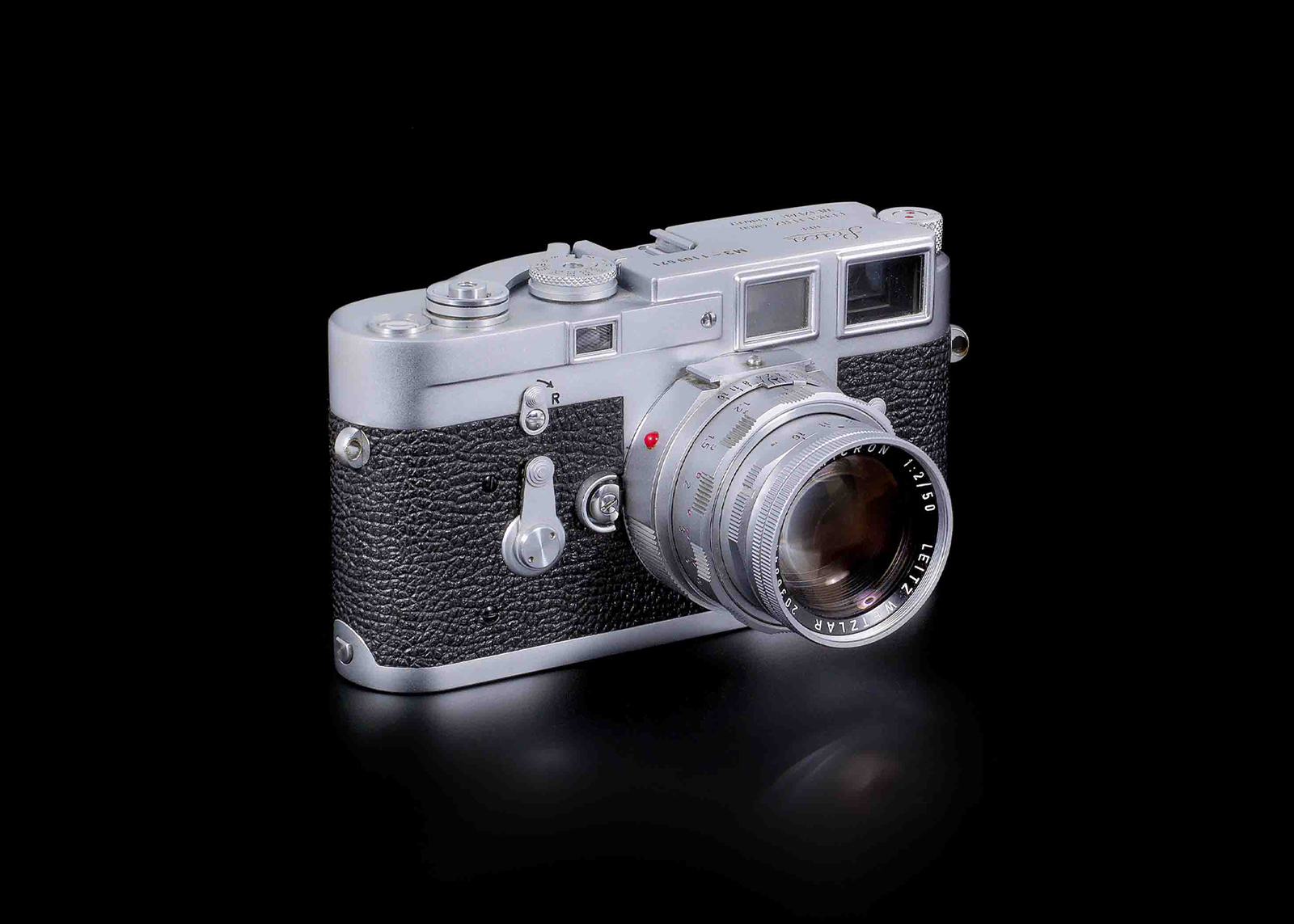 Vintage silver Leica camera with textured black grip and attached lens on black background.