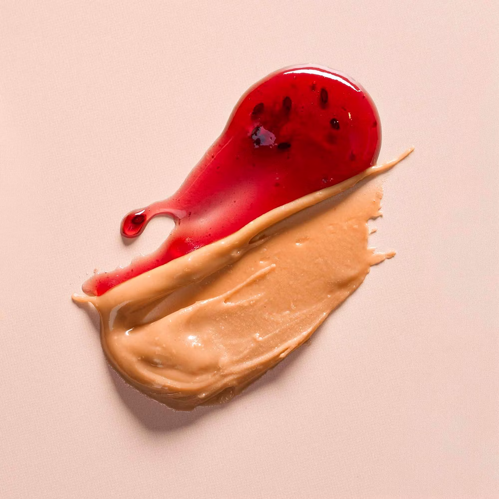Spoonful of peanut butter and red jelly side by side on a pale surface.