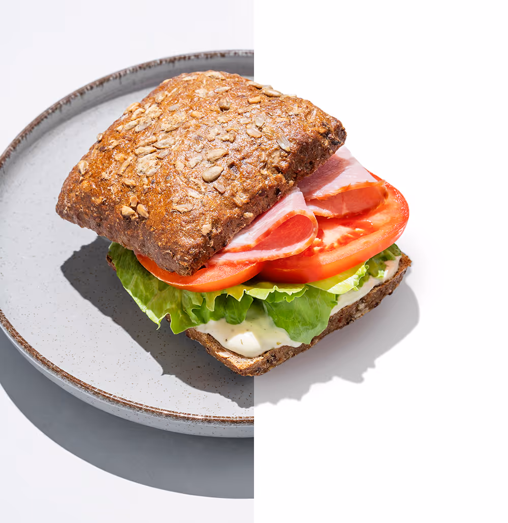 Ham sandwich with lettuce and tomato on seeded whole grain bread on a speckled ceramic plate.