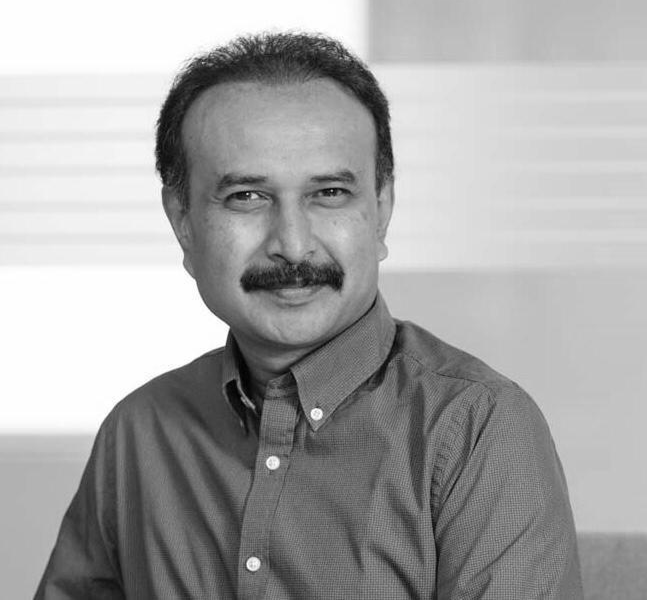 Portrait of a middle-aged man with a mustache, wearing a buttoned-up checkered shirt, smiling slightly at the camera.