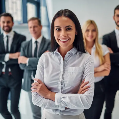 Smiling businesswoman standing confidently with arms crossed in front of four colleagues in an office.