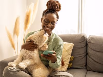 Woman sitting on the sofa with her dog, using her phone.