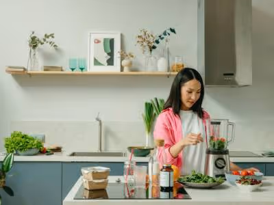 Woman preparing food in the kitchen, standing at a blender.
