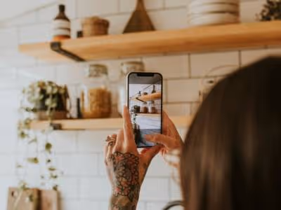 Woman taking photo of her kitchen shelves, using her smartphone.