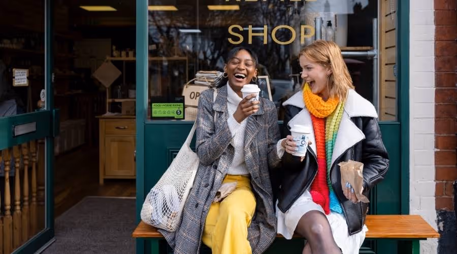 two friends drinking take away coffee outside a store.