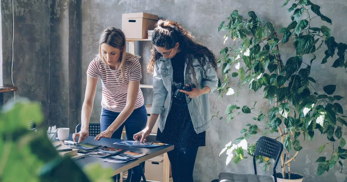 Two friends looking at designs while standing in front of a table.