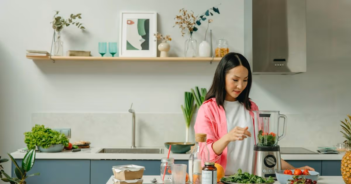 Woman preparing food in the kitchen, standing at a blender.