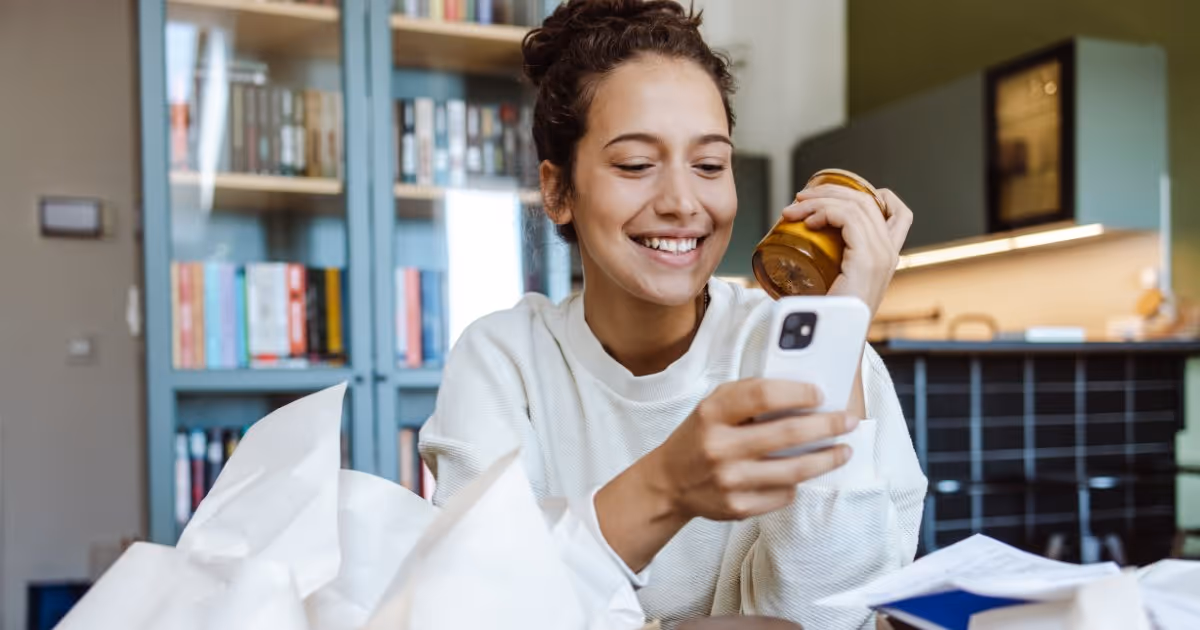 Woman unpacking a product in her kitchen while also using her phone.