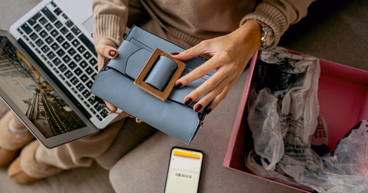 Overhead view of a woman looking at her new purse, with a laptop on her lap and her phone on the side. 