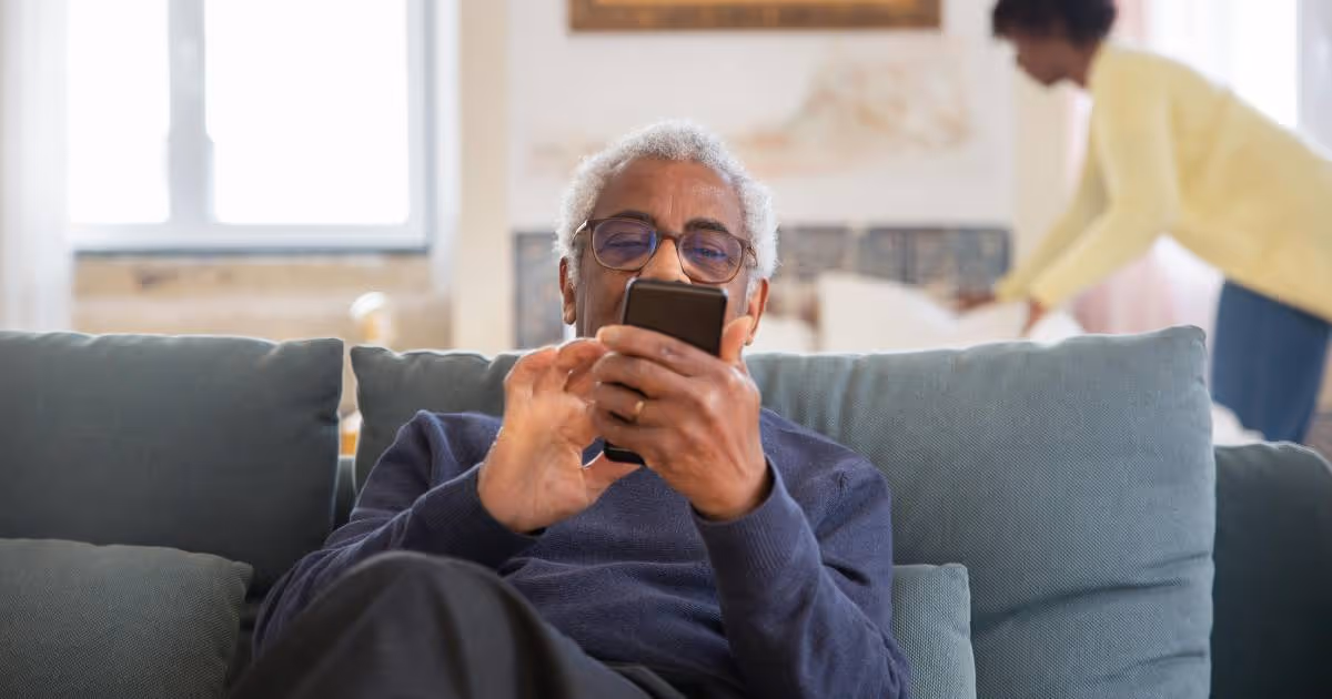 Elderly man using phone while sitting on sofa.