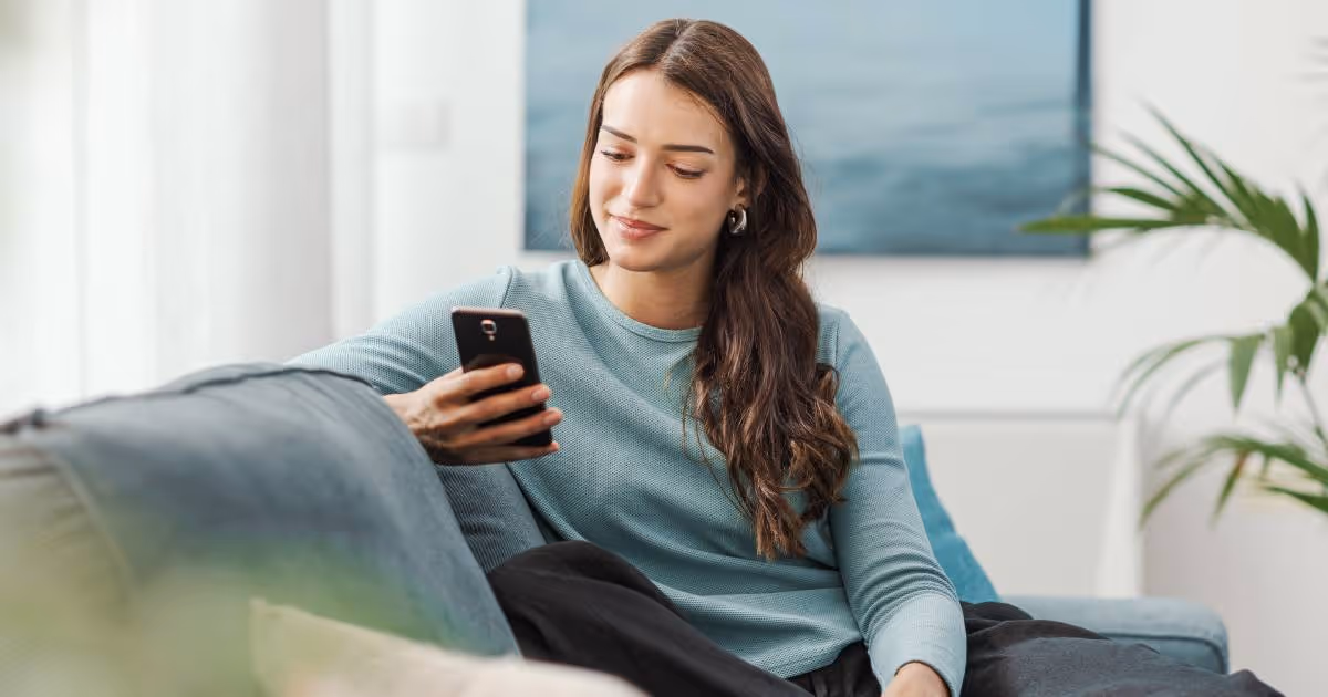 Woman sitting on sofa at home using her phone.