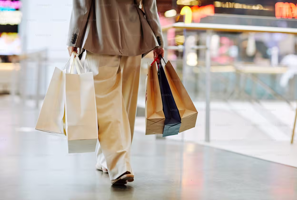 Close up of a person walking through a shopping mall, with only their legs in shot, while holding shopping bags.