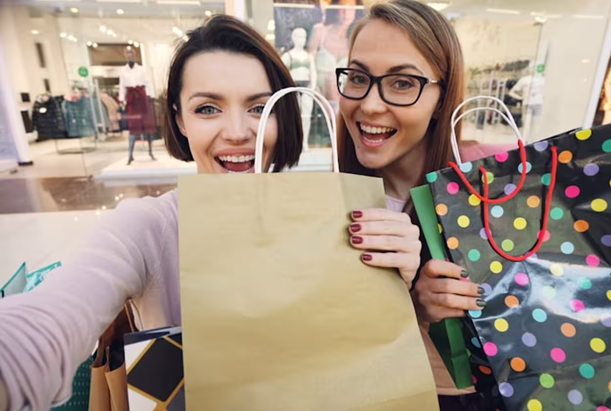 Two young girl friends posing for a selfie with their shopping bags.