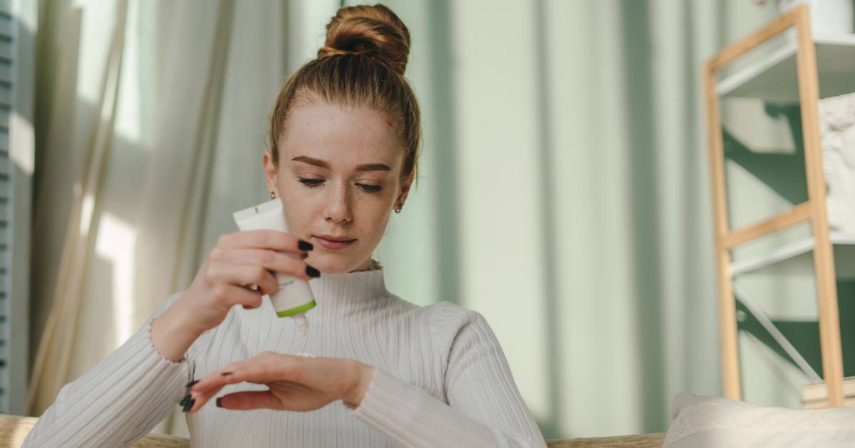 Young woman testing skincare, pouring the bottle contents on her hand.