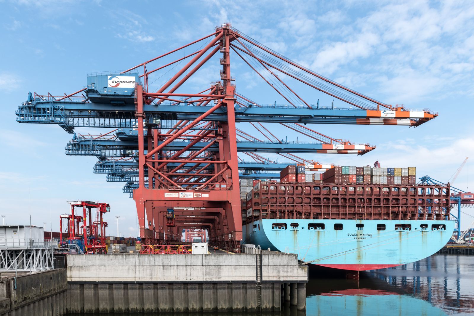 Gantry cranes working a Maersk container ship alongside a terminal quay, containers stacked on deck