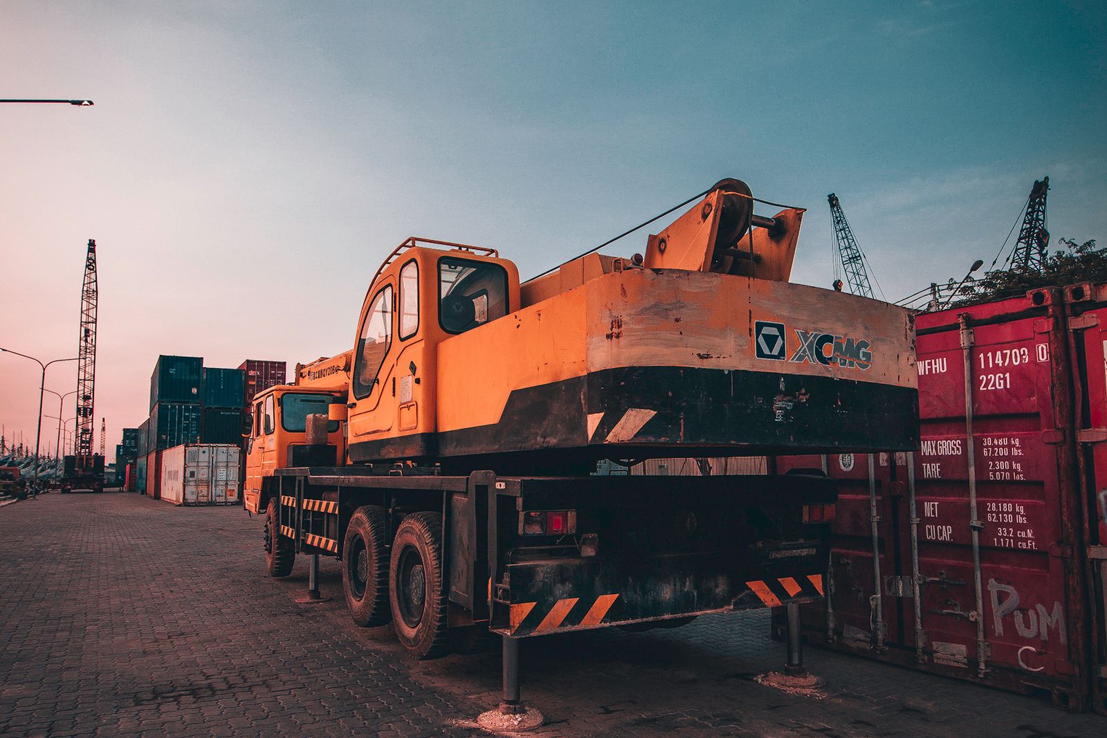 A mobile crane parked beside a shipping container whose door displays its maximum gross weight, tare weight and net weight in kilograms and pounds.