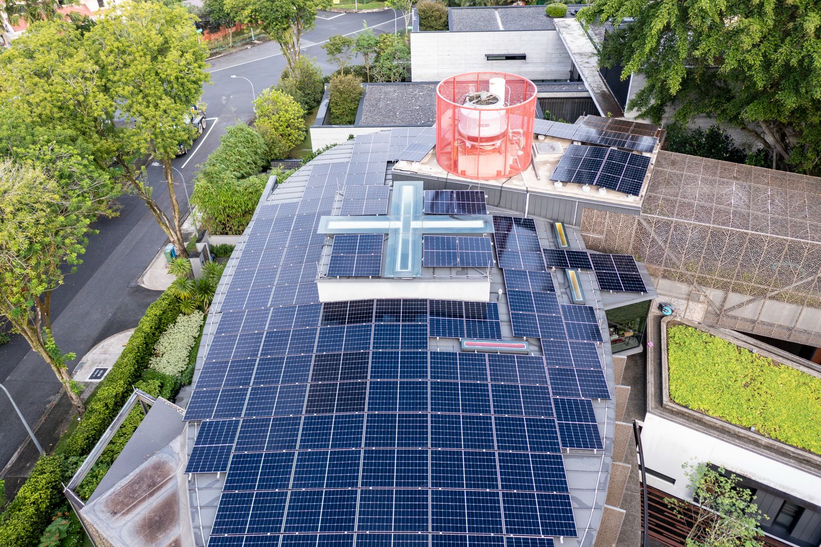 Aerial view of a 49.02 kWp solar panel installation on a curved metal roof Good Class Bungalow at Gallop Park, Singapore, showing near-total roof coverage with panels arranged around a distinctive cross-shaped skylight on an organically shaped roofline