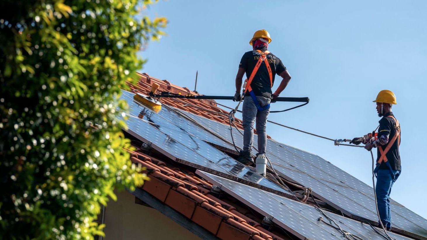 Two harnessed technicians performing solar panel maintenance and cleaning to remove dirt on a Singapore landed home tiled roof
