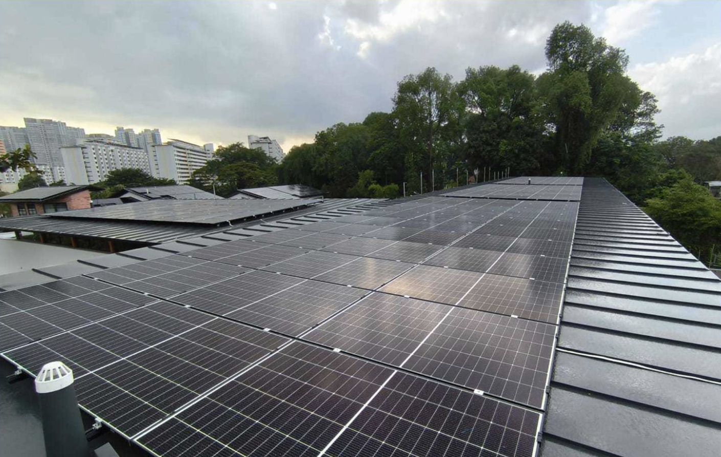 Aerial view of a 57.33 kWp Trina solar panel array on the metal roof of a Good Class Bungalow off Holland Road (District 10, Singapore), with HDB blocks and mature trees in the background.