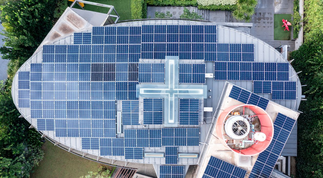 Aerial view of a large rooftop solar panel installation on a landed home at Gallop Park, Singapore, with panels arranged around a cross-shaped skylight on an oval roof