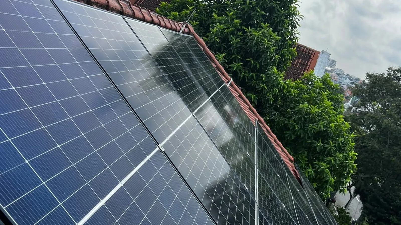 Monocrystalline solar panels on a terracotta-tiled roof in Singapore under a cloudy tropical sky, where heat and humidity shape panel lifespan and degradation.