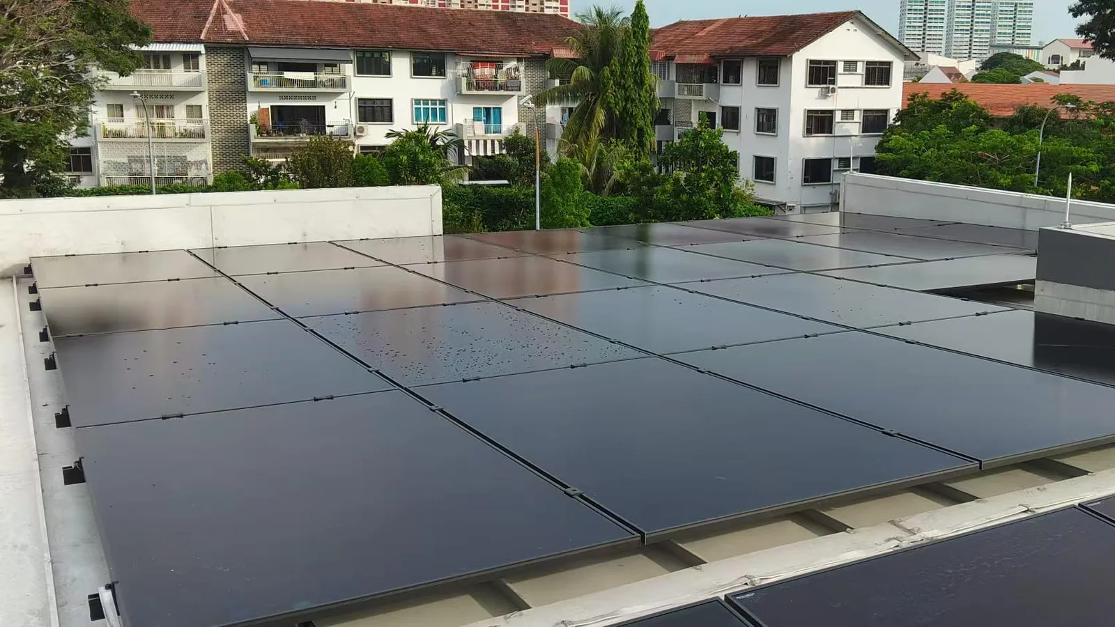 Solar panels on the flat roof of a Singapore home with walk-up flats behind, generating surplus electricity that is exported to the grid for credits.