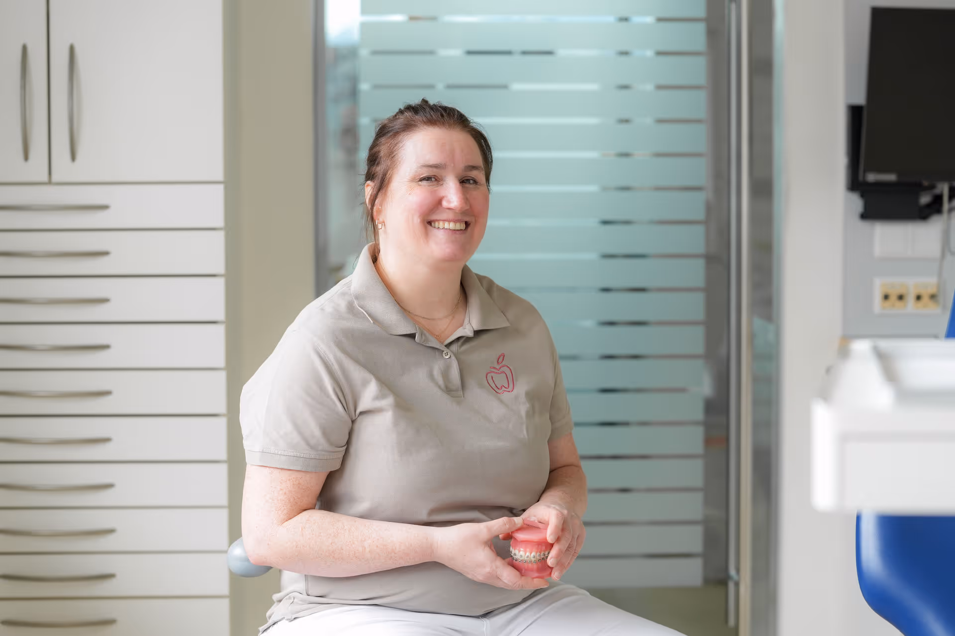 Zahnärztin lächelt und hält ein kieferorthopädisches Modell mit Zahnspange in einer Praxis.