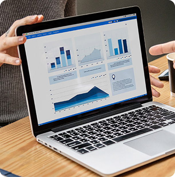 Person holding a laptop displaying multiple blue-toned bar and line charts on a wooden table.