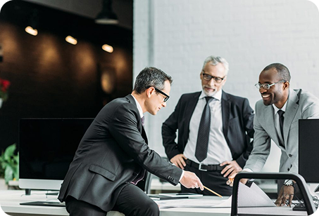 Three professionally dressed men in an office discussing documents on a table, with one man pointing at papers.