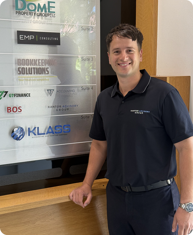 Man wearing a black polo shirt with 'Kantor Advisory Group' stands smiling next to a business directory listing multiple companies.