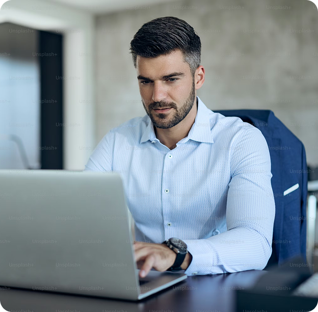 Focused man in a light blue shirt working on a laptop at a desk in a modern office.