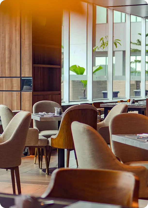 Interior of a modern restaurant with cushioned chairs, wooden tables, and large windows letting in natural light.