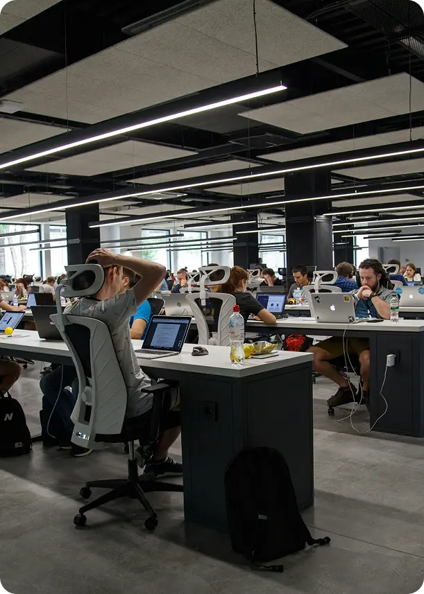 People working on laptops in a modern, open-plan office with white desks and ergonomic chairs.