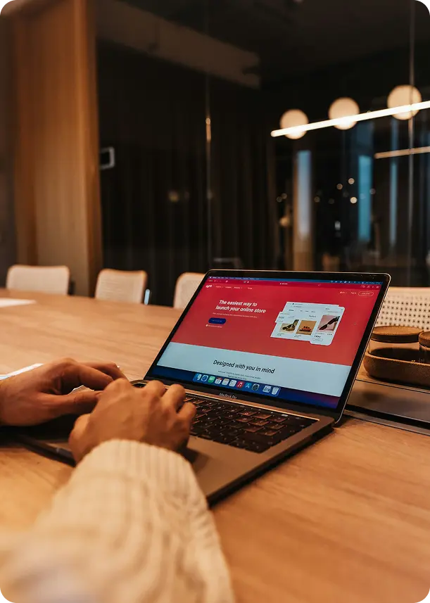 Person typing on a laptop displaying a website builder interface with red header text about launching an online store.