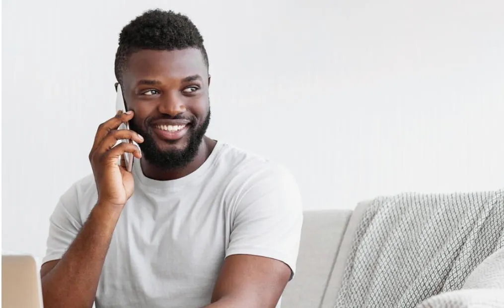 Smiling young man sitting on a couch talking on a smartphone.