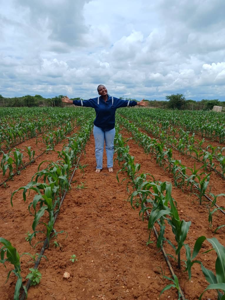 Woman standing with arms outstretched in a field of young green crops under a cloudy sky.