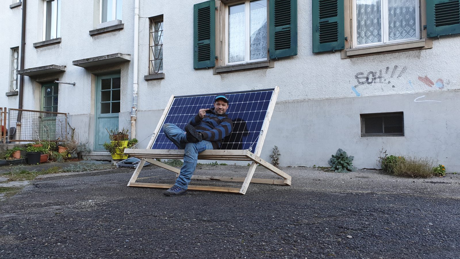 Solarmaa-Mitarbeiter sitzt entspannt auf einem Liegestuhl, der aus einem Solarmodul gebaut ist, vor einem Schweizer Wohnhaus in Biel — humorvolle Solarmaa-Antwort auf Trumps Aussage zu Öl- und Gasheizungen.