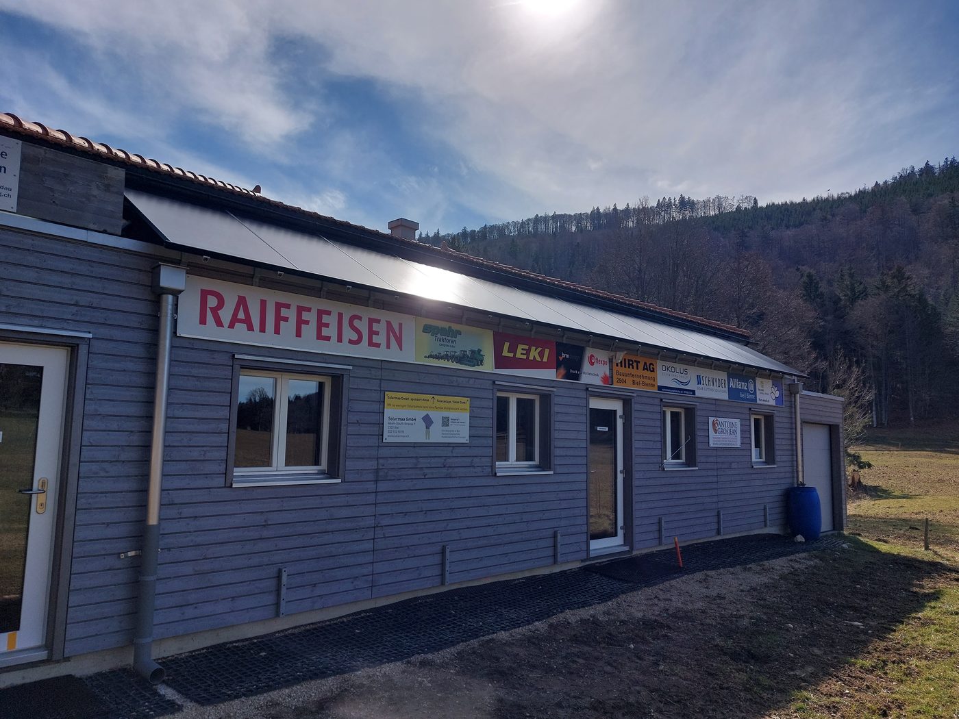 Seitliche Ansicht des Langlaufzentrums Près d’Orvin: die Solaranlage bildet den optischen Übergang von der Fassade zum Ziegeldach