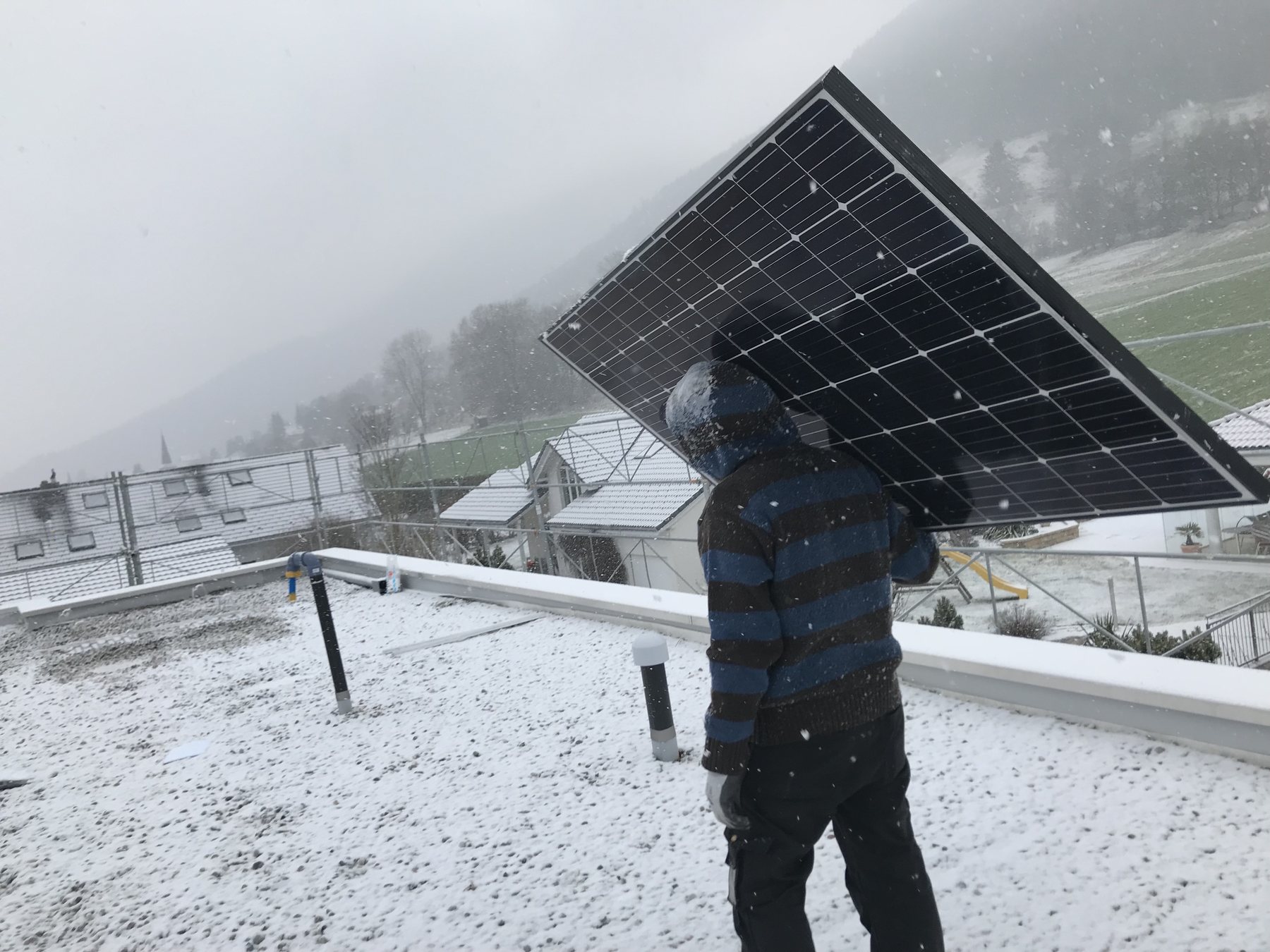 Solarmaa-Monteur trägt Solarmodul bei Schneefall aufs Dach
