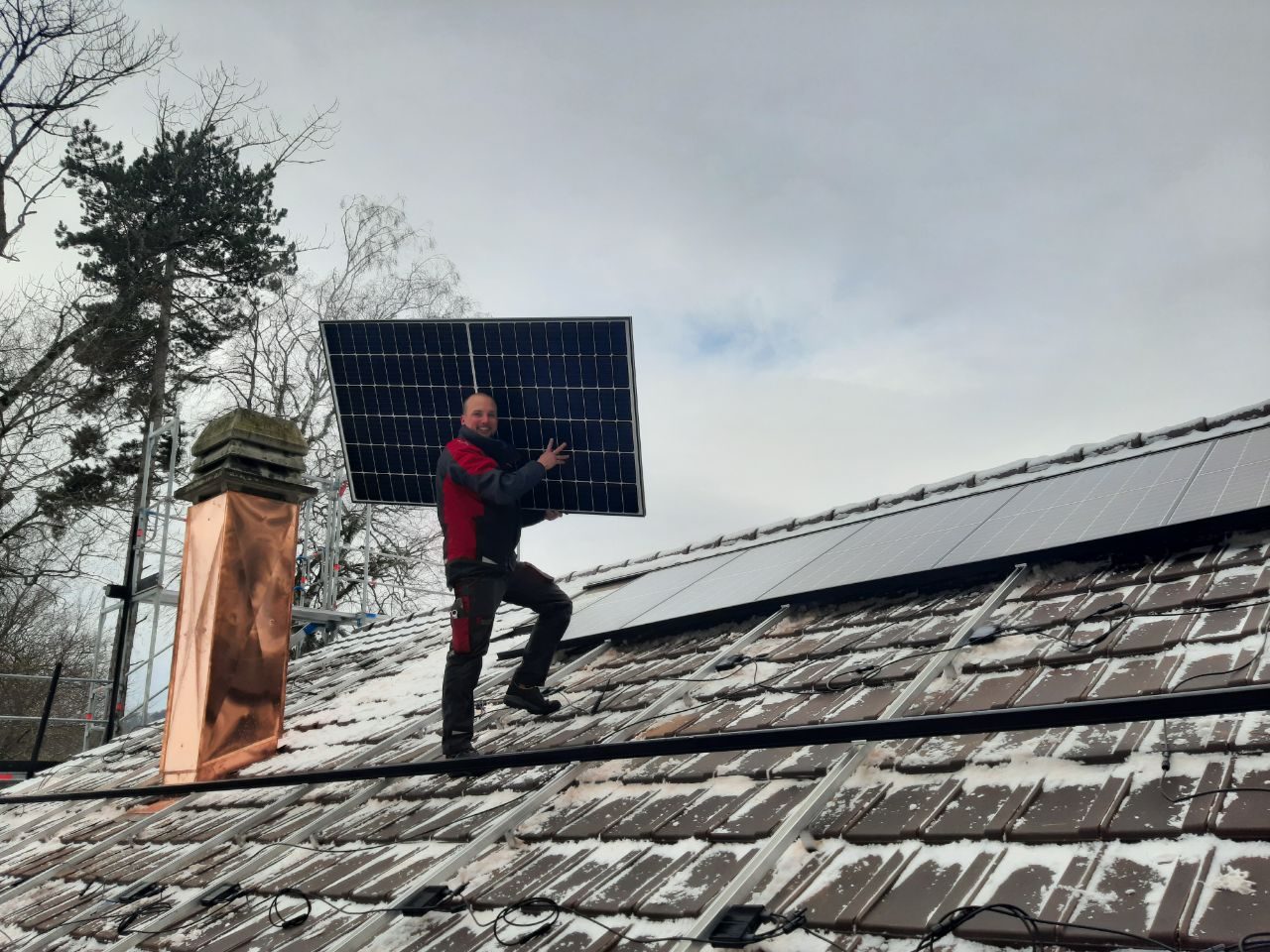 Solarmaa-Monteur trägt ein Solarmodul über das verschneite Ziegeldach