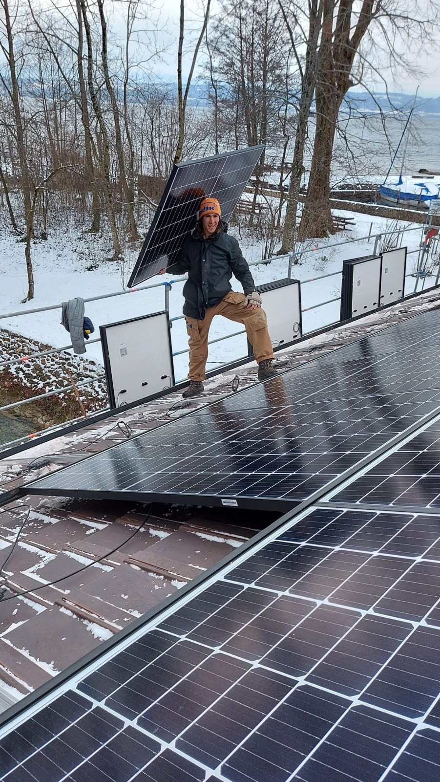Solarmaa-Monteur trägt ein Solarmodul über ein verschneites Dach am Bielersee