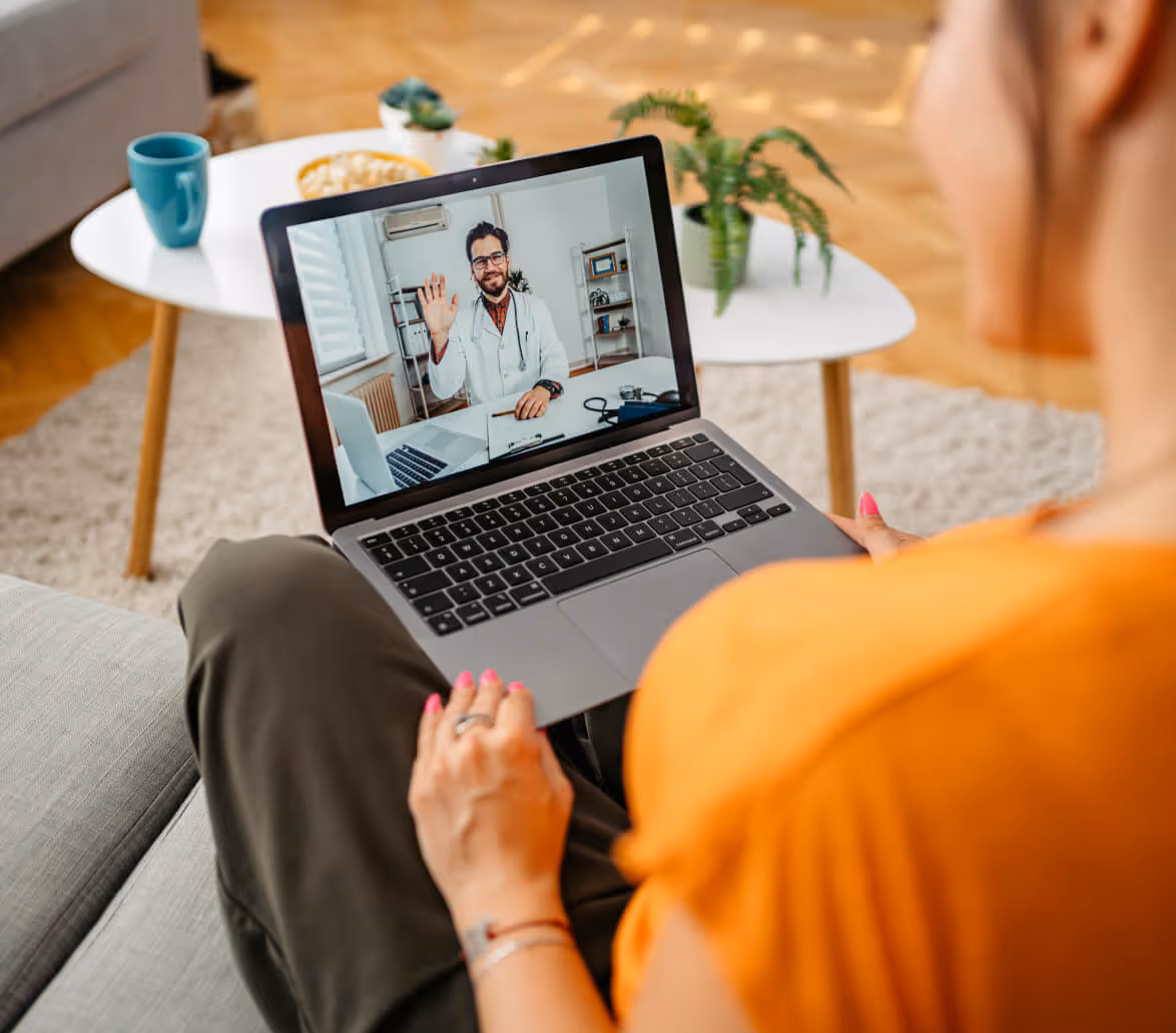 Person holding a laptop video calling a male doctor who is waving on the screen.