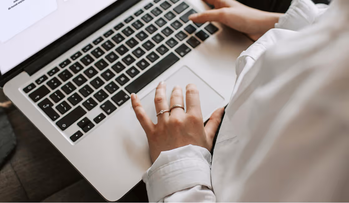 Person wearing a white shirt typing on a silver laptop keyboard with two rings on their left hand.