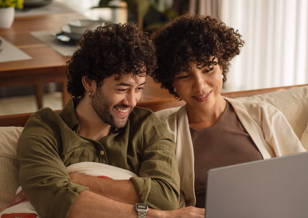 Smiling young couple with curly hair sitting on a couch looking at a laptop.