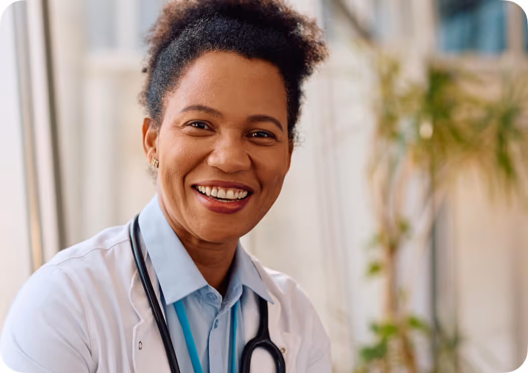 Smiling female doctor with curly hair wearing a white coat and stethoscope.