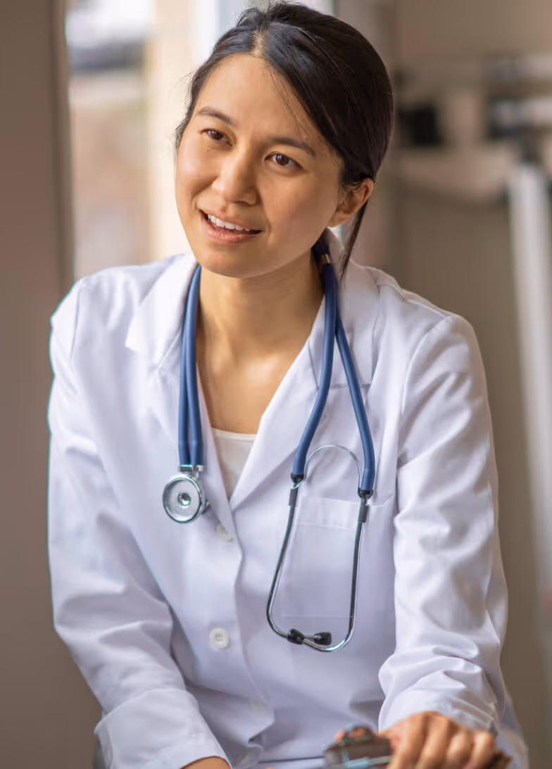 Female doctor wearing a white coat and blue stethoscope speaking with a patient.