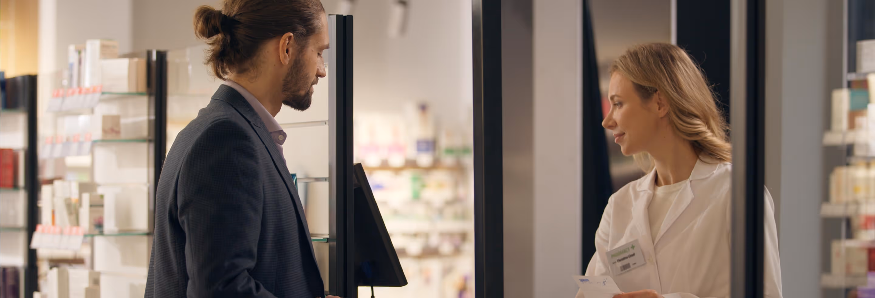 Man in suit interacts with a female pharmacist behind the counter in a pharmacy.